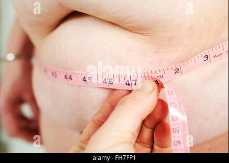 Infermiera in ospedale locale utilizzando un nastro di misurazione per calcolare il BMI e misurare il peso dei pazienti e lo stomaco Foto Stock