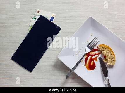 Piastra vuota a sinistra dopo la cena con Bill e Euro nota sul tavolo di legno Foto Stock