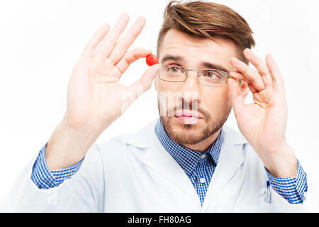 Giovane maschio medico in bicchieri guardando sulla pillola isolato su uno sfondo bianco Foto Stock
