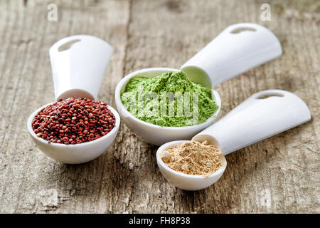 Sessole per misurazione con orzo o erba di frumento polvere, rosso di quinoa e polvere di maca sul tavolo di legno Foto Stock