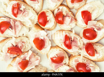 Gustosi crostini con burro, prosciutto e pomodori ciliegini. Tema alimentare. Rinfreschi per gli ospiti. Foto Stock