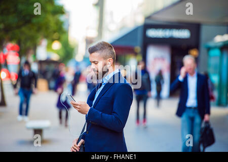 Manager con lo smartphone ascoltando musica fuori in strada Foto Stock