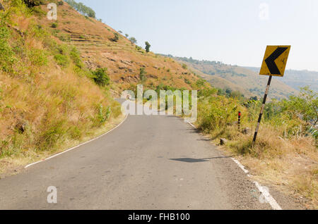 Freccia sinistra strada segno lungo la curva di una strada di montagna in Panchgani, Maharashtra, India. Foto Stock
