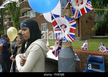 Una giovane donna musulmana che indossa un capo sciarpa in piedi accanto a una bandiera dell'Union Jack a Golden Jubilee Street party in Jubilee Street in Stepney Green area di East London, dove centinaia di persone ha festeggiato i 50 anni di regno della regina Elisabetta II. Le celebrazioni hanno avuto luogo in tutto il Regno Unito con il fulcro di una parata e fuochi d'artificio a Buckingham Palace, Regina della residenza di Londra. La regina Elisabetta salì al trono britannico nel 1952 in seguito alla morte di suo padre, il re George VI. Foto Stock