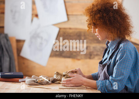 Profilo di focalizzata redhead donna giovane ceramista creazione utilizzando scultura in argilla nel laboratorio di ceramica Foto Stock