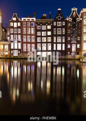 Edifici antichi lungo Damrak ad Amsterdam di notte. Riflessioni può essere visto nell'acqua. Foto Stock