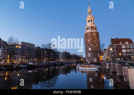 Una vista lungo il canale Oudeschans verso la Torre Montelbaanstoren ad Amsterdam al crepuscolo. Edificio, barche e riflessioni Foto Stock