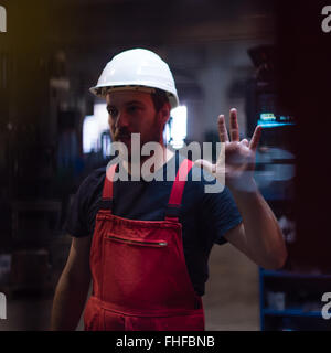 Dynamic close-up di un lavoratore che indossa tuta rossa e bianca di un casco di protezione, con la sua mano sinistra sollevata, mostrando la sua sinistra rin Foto Stock