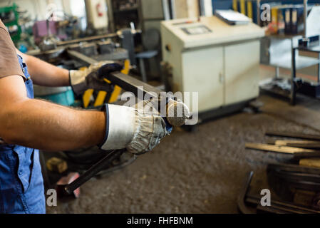 Close-up di un uomo con le mani in mano in bianco heavy-duty guanti, azienda e l'esame di una tubazione quadrata, in un capannone industriale, con metallurg Foto Stock