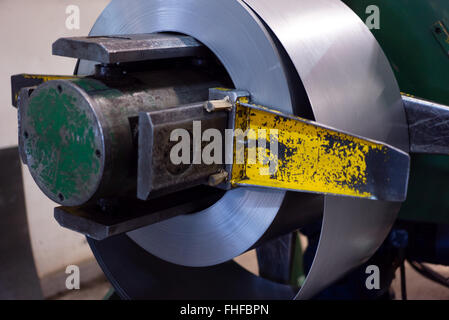 Close-up di rotolo di lamiera il dispiegamento da una parte girevole, la quale è attaccata ad un heavy-duty macchina verde, in un capannone industriale Foto Stock