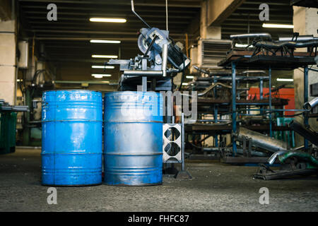 Vista dei due blu barili industriali con la vernice consumata, prevista in posizione verticale sul piano di un capannone industriale, con ripiani pieni Foto Stock