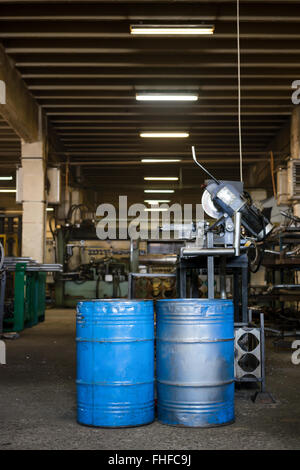 Vista dei due blu barili industriali con la vernice consumata, prevista in posizione verticale sul piano di un capannone industriale, con ripiani pieni Foto Stock