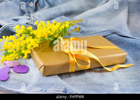 Bouquet di mimosa pudica e un avvolto presente sul jeans blu Foto Stock