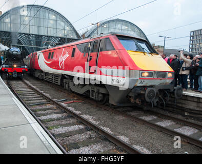 La stazione di Kings Cross, London, Regno Unito. Il 25 febbraio 2016. Una moderna classe vergine 91 foglie elettrico piattaforma 2 prima della mitica locomotiva a vapore Flying Scotsman si allontana dalla stazione Kings Cross Platform 1 a 07.40am per un viaggio inaugurale celebrativo correre lungo la costa Est Mainline dopo una lunga decade 4.2million pound restauro. Questo viaggio storico, tra Londra e York, è la prima occasione per il pubblico di vedere l'amata motore in verde e porta la sua iconica targhetta di fabbrica. Credito: Malcolm Park editoriale/Alamy Live News Foto Stock