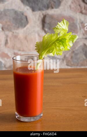 Bicchiere di succo di pomodoro con un gambo di sedano seduto su un tavolo in legno nella parte anteriore di un rustico muro di pietra Foto Stock