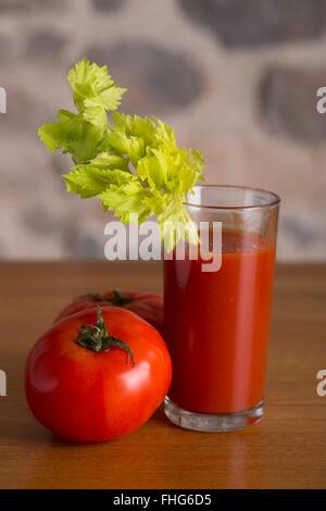 Bicchiere di succo di pomodoro con un gambo di sedano e un paio di carni bovine fresche pomodori in un paese tavolo da cucina con un muro di pietra Foto Stock