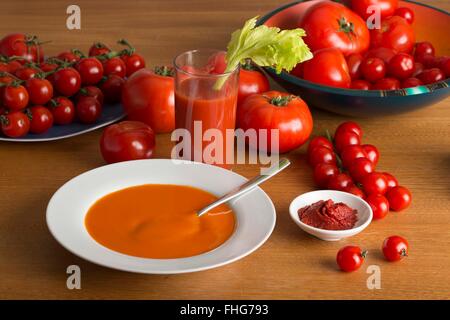 Minestra di pomodoro, un bicchiere di succo di pomodoro e un piatto di concentrato di pomodoro circondato da un sacco di pomodori freschi di diverse dimensioni Foto Stock