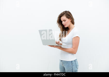 Giovane bella donna moderna avente un computer portatile in mani, poggiando su una parete bianca, felice Foto Stock