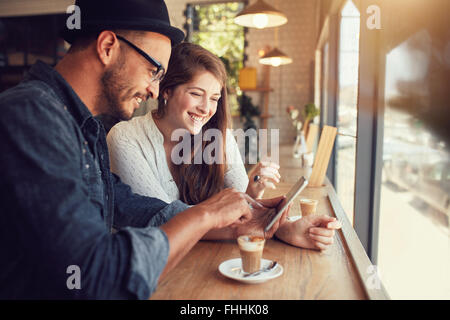 Coppia felice in una caffetteria navigando in internet sulla tavoletta digitale. Giovane uomo e donna in un ristorante guardando il touch screen co Foto Stock