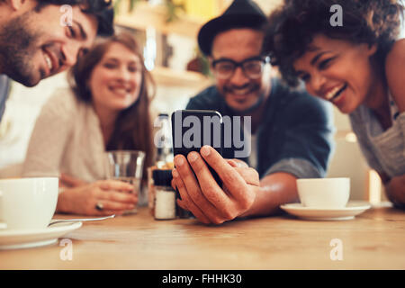 Gruppo di amici divertendosi al cafe e guardando a smart phone. Uomo che mostra qualcosa ai suoi amici seduti da, focus su mo Foto Stock