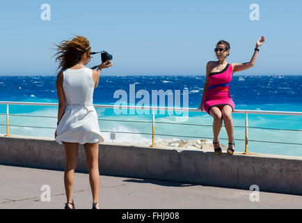 Due amiche scattando foto di ogni altro come essi pongono accanto al mare di Nizza, Francia Foto Stock