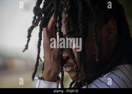 Un afro-americano di adolescente con dreadlocks si erge contro una parete di stagno/siede nel sedile posteriore di un Impala in a junkyard in NC. Foto Stock