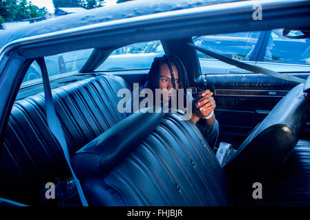 Un afro-americano di adolescente con dreadlocks si erge contro una parete di stagno/siede nel sedile posteriore di un Impala in a junkyard in NC. Foto Stock