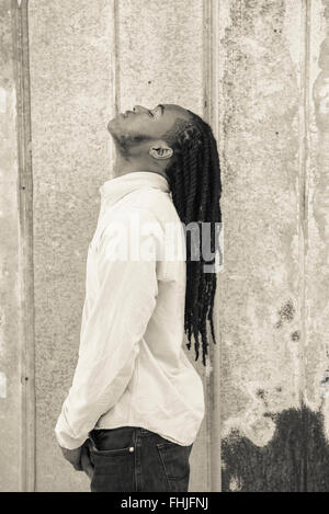 Un afro-americano di adolescente con dreadlocks si erge contro una parete di stagno/siede nel sedile posteriore di un Impala in a junkyard in NC. Foto Stock