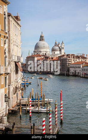 Il Canal Grande, i bastoncini d'ormeggio rossi e bianchi e la Basilica di Santa Maria della Salute dal Ponte dell'Accademia, Venezia, Italia sotto un cielo blu Foto Stock