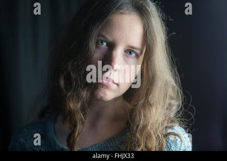 Fair-pelato donna con ondulazione/curly marrone capelli, occhi blu e espressione seria nella drammatica illuminazione studio Foto Stock
