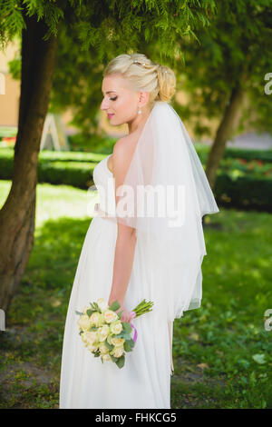 Sposa in abito bianco in piedi vicino al parco di alberi Foto Stock