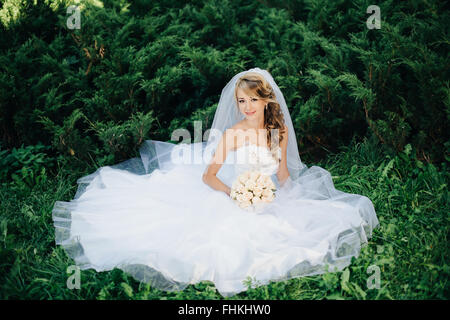 Sposa seduta su erba verde in posizione di parcheggio Foto Stock
