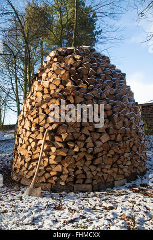 Un ascia in legno appoggiata contro un Holz Hausen pila di legno nella neve. Foto Stock