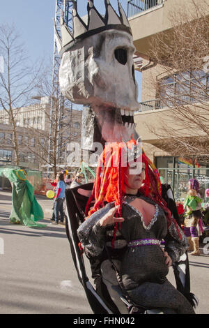 Un enorme cranio puppet toothily sorrisi dietro una donna vestita di un costume colorato in Asheville Mardi Gras Parade Foto Stock