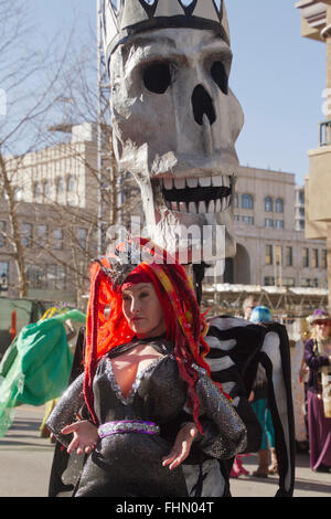 Un enorme cranio puppet toothily sorrisi dietro una donna vestita di un costume colorato in Asheville Mardi Gras Parade Foto Stock