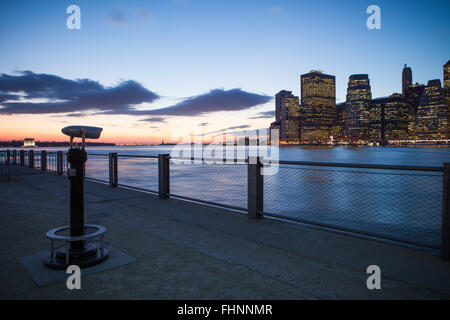 Un telescopio punti verso Manhattan inferiore attraverso il fiume di Brooklyn al tramonto Foto Stock