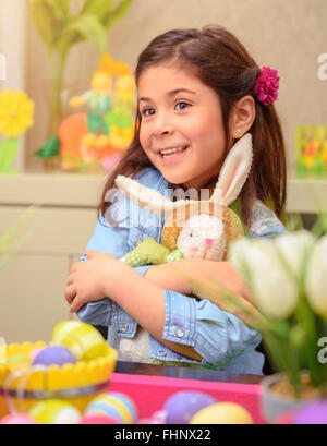 Ritratto di adorabile bambina con piacere che abbraccia il suo amico, giocattolo morbido coniglietto di Pasqua, divertendosi a casa Foto Stock