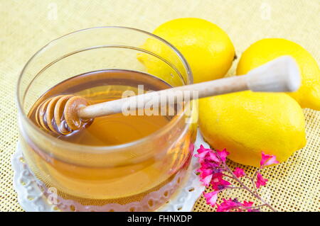 Un vasetto di miele con un bilanciere di legno cucchiaio e limoni Foto Stock