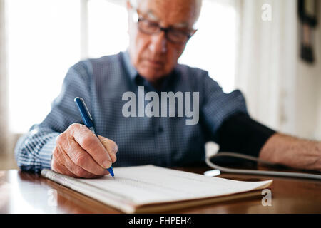 Uomo senior di controllare la sua pressione del sangue e scrivendo il risultato, close-up Foto Stock