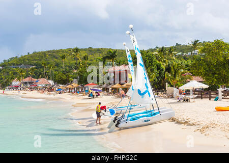 Vista panoramica di Dickenson Bay, a nord Antigua, con ombrelloni e sedie a sdraio e sandali barche a vela sulla spiaggia Foto Stock