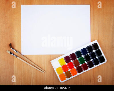 Foglio di carta bianco con acquarello e spazzole su un tavolo di legno Foto Stock