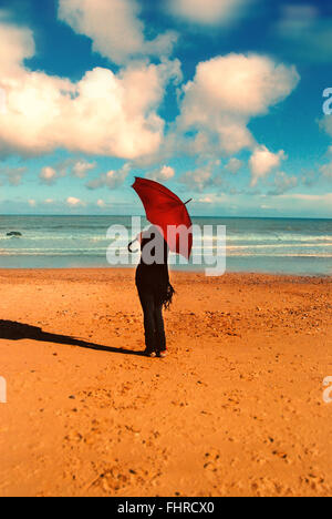 Donna con ombrello rosso permanente sulla spiaggia Sunny Beach Foto Stock