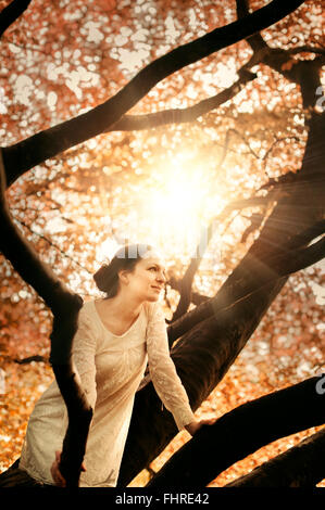 Giovane bella donna seduta sul ramo di albero Foto Stock