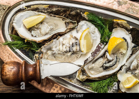 Aprire le ostriche con un pezzo di limone su cooper vassoio. Foto Stock