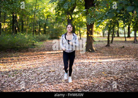 Montare la donna a fare jogging nel parco circondato da alberi verdi Foto Stock