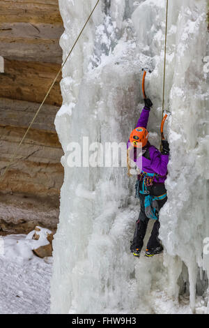 Donna ice climber salendo una cascata ghiacciata in Pictured Rocks National Lakeshore, Penisola Superiore, Michigan, Stati Uniti d'America Foto Stock