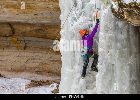 Donna ice climber salendo una cascata ghiacciata in Pictured Rocks National Lakeshore, Penisola Superiore, Michigan, Stati Uniti d'America Foto Stock