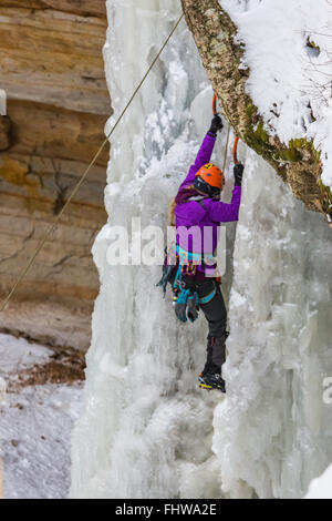 Donna ice climber salendo una cascata ghiacciata in Pictured Rocks National Lakeshore, Penisola Superiore, Michigan, Stati Uniti d'America Foto Stock