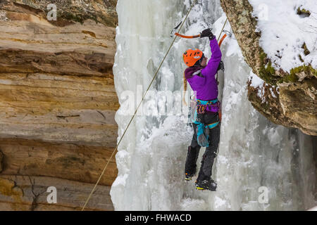 Donna ice climber salendo una cascata ghiacciata in Pictured Rocks National Lakeshore, Penisola Superiore, Michigan, Stati Uniti d'America Foto Stock