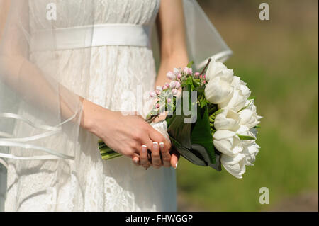 Mano di donna detiene il bouquet di tulipani bianco e la fioritura di ciuffo di Apple su sfocato sfondo verde nella soleggiata giornata di primavera. Foto Stock